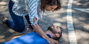 Rescuer checking an unconscious person's responsiveness by gently tapping the shoulders before starting CPR in an outdoor emergency.