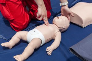 Rescuer checking the brachial pulse of an infant CPR training mannequin before initiating infant cardiopulmonary resuscitation.